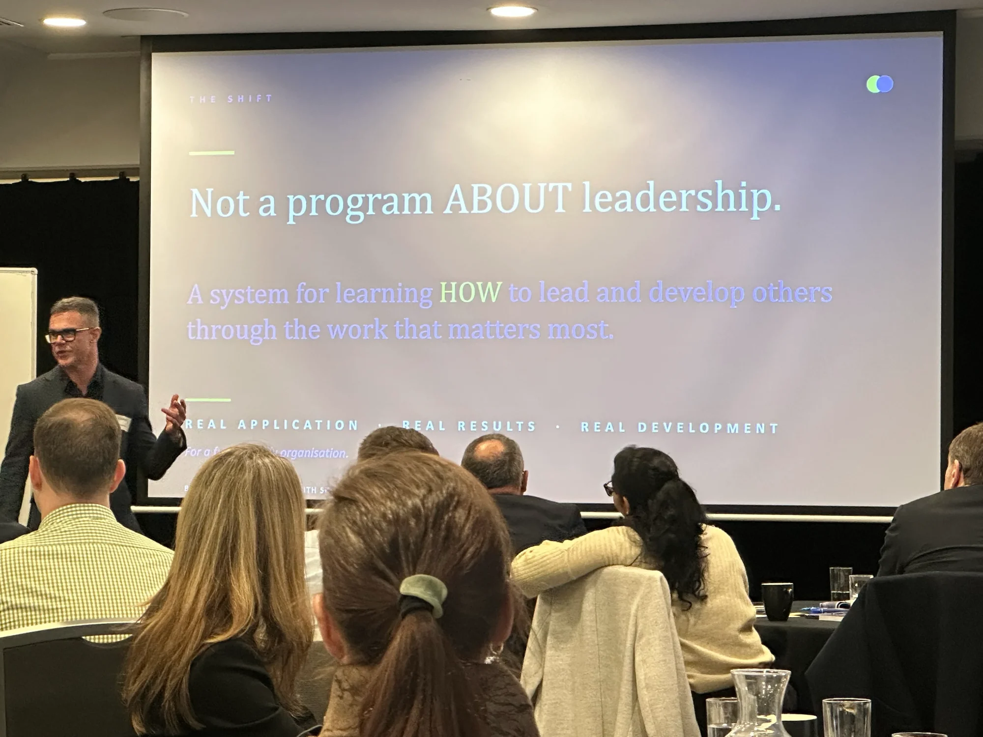 Benny Ausmus speaking to an audience in front of a presentation slide